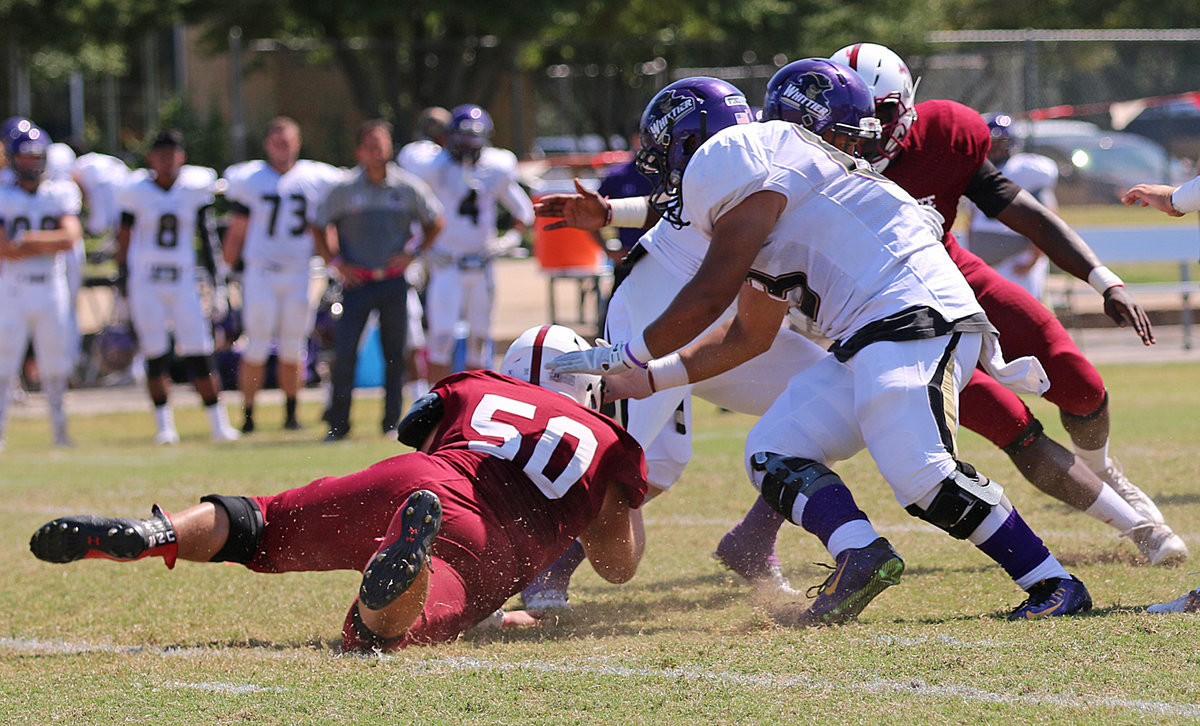 Image: Austin College junior nose guard Zain Byers (#50 in Crimson) latches on to a Whittier Poet running back.